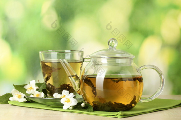 绿茶与茉莉花在杯子和绿色背景上的木桌上的茶壶