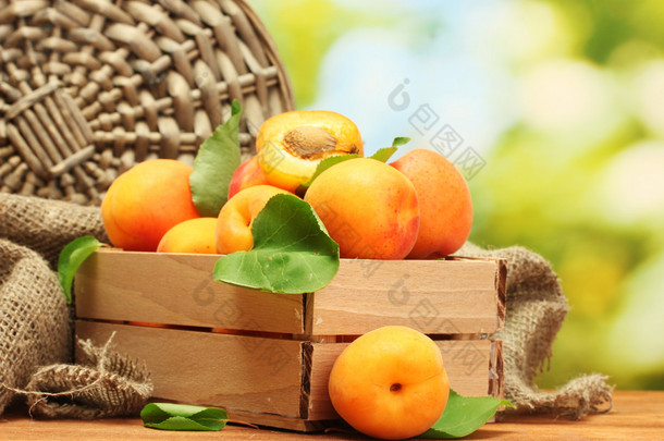 成熟的杏树，叶在木盒中，绿色背景的木制桌子上