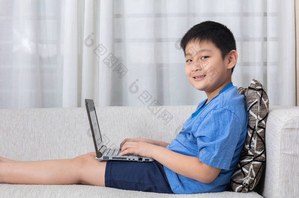 在沙发上使用笔记本电脑的快乐亚洲中国小男孩