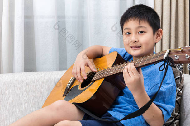 快乐亚洲<strong>中国</strong>小男孩坐在沙发上弹吉他
