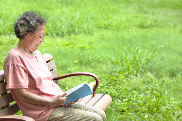 快乐的高级女人坐在长凳上，和读一本书