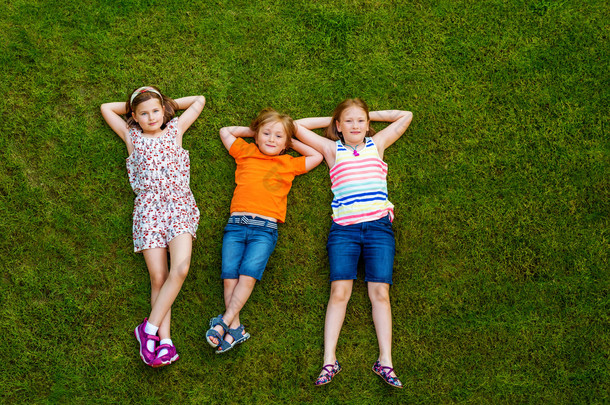 快乐的孩子们在户外玩得开心。孩子们在夏天公园玩。小男孩和两个女孩躺在绿色的鲜草