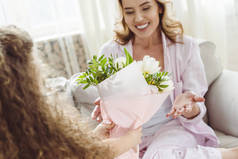 女儿在母亲节快乐的母亲面前献上花束给她微笑的妈妈。