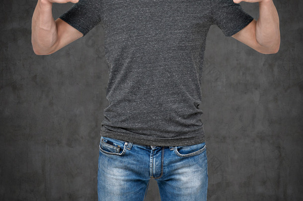 Close-up of a man pointing his fingers on a blank grey t-shirt. Dark concrete background.