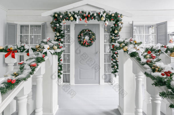 圣诞节早晨。为假日装饰的房子入口。圣诞装饰。冷杉树枝的花环和栏杆上的灯