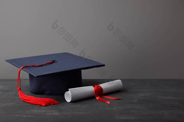 文凭和学术盖帽与<strong>红色</strong>流苏在黑暗的表面在灰色