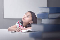 快乐的亚洲小女孩用书本和钢笔思考