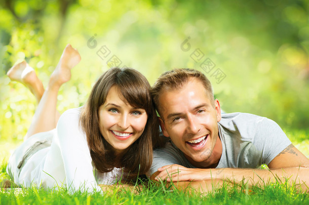 快乐的新人面带笑容一起躺在户外的绿草上