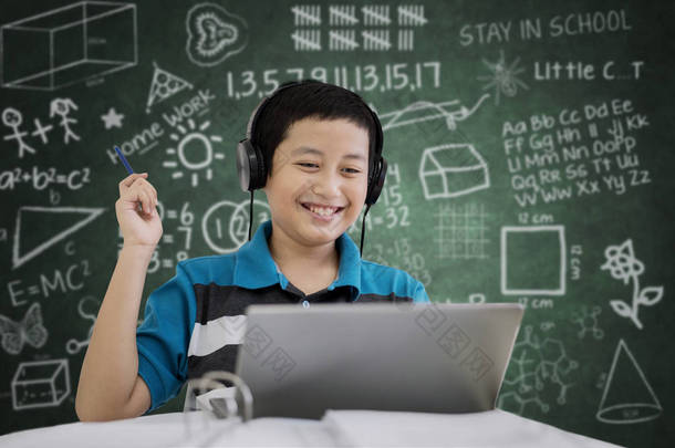 青春期学生用笔记本电脑学习时的图片在黑板上涂鸦的教室里听音乐