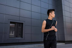 年轻亚洲运动员在耳机奔跑在城市街道