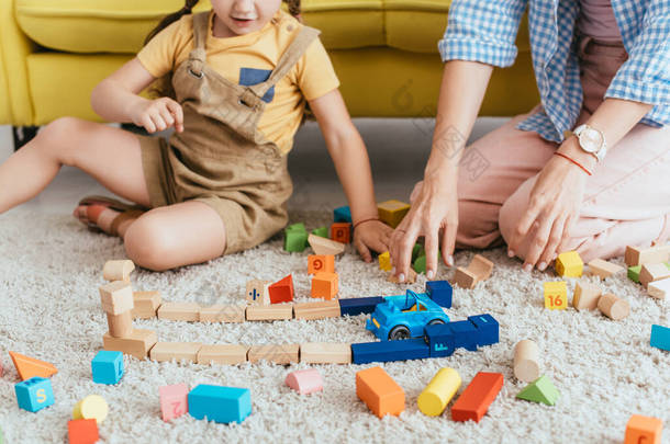 儿童和<strong>护士</strong>在地板上玩五颜六色的方块和玩具车的局部视图