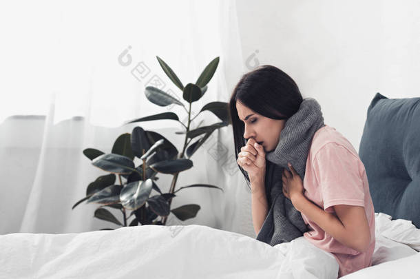 生病的年轻妇女坐在<strong>床上</strong>咳嗽, 而痛苦喉咙痛