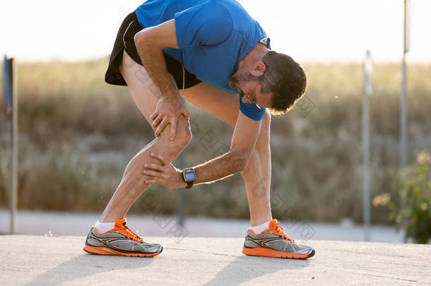 有强壮运动腿的年轻运动男子膝盖与他的手在肌肉受伤后疼痛在沥青路面运动训练中的肌肉或韧带损伤概念.