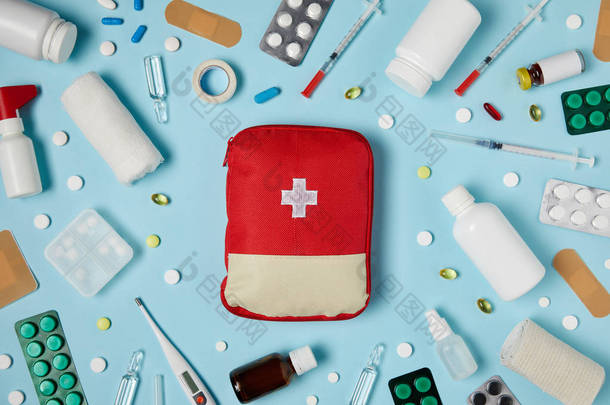 红色急救包袋在蓝色表面被不同的药物包围的顶部视图