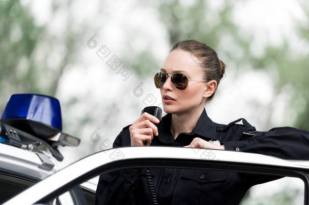 有吸引力的女警察在警车附近讲话由收音机设置