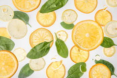 明亮的橘子和柠檬片与绿色菠菜叶在灰色背景