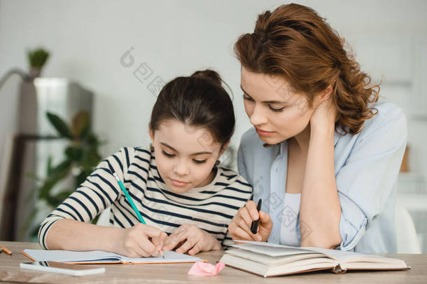 有吸引力的女人帮助集中的女儿在家里做功课
