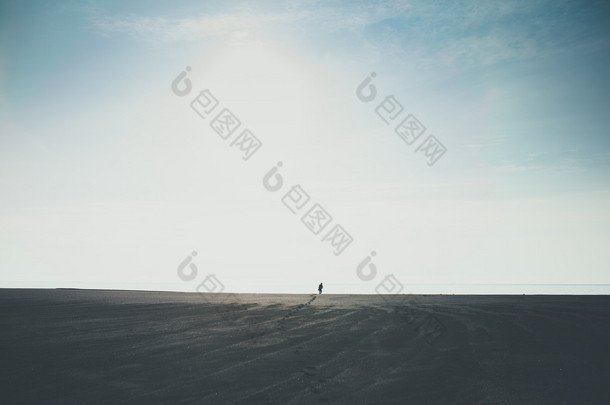 男子独自走到地平线在冰岛的黑色沙滩上留下脚印