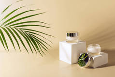 关闭绿色棕榈叶, 面部和身体霜的玻璃罐子上的白色立方体上米色背景