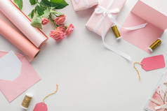 灰色背景上的粉红色玫瑰、纸卷、包装礼品、信封和贺卡的顶视图 