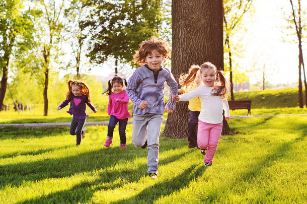许多年幼的孩子微笑着沿着公园的草地奔跑。.
