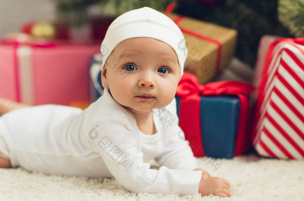 特写肖像可爱的小婴儿躺在地板上的圣诞礼物模糊的背景和看着相机