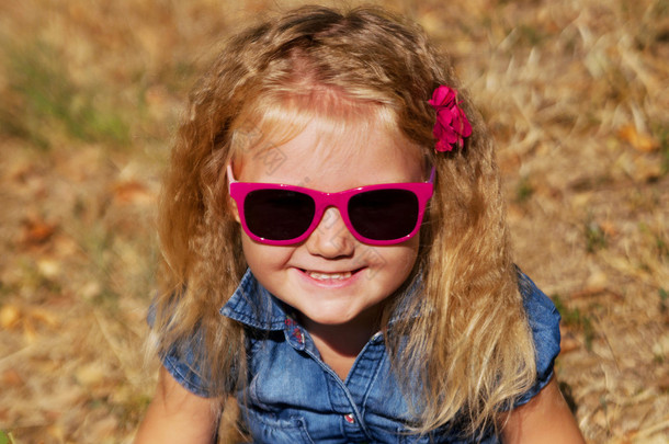 小女孩坐在粉红色的太阳镜看起来和微笑