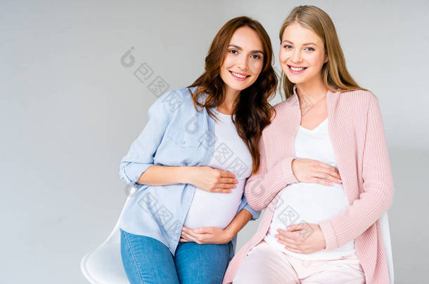 <strong>怀孕</strong>的微笑的妇女坐在椅子上孤立的灰色