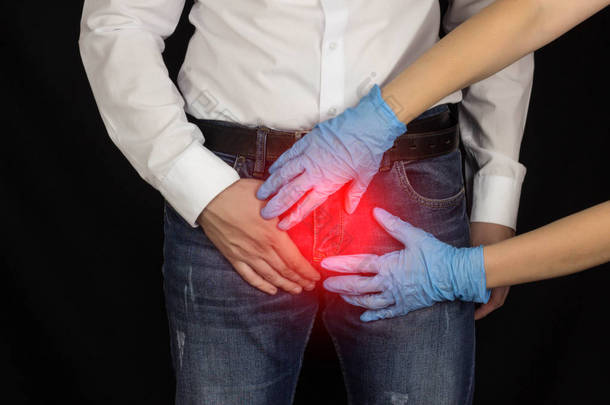 一个穿牛仔裤和白衬衫的男人正抱着腹股沟, 戴着医疗手套的女人手里握着一个男人的腹股沟。黑色背景, 前列腺炎