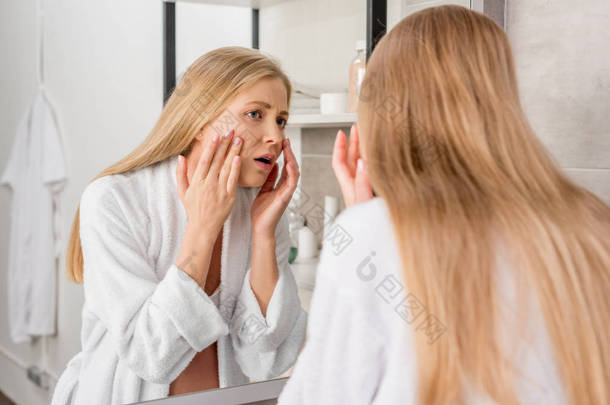 有皮肤问题的成人怀孕妇女通过镜子在浴室看她的脸
