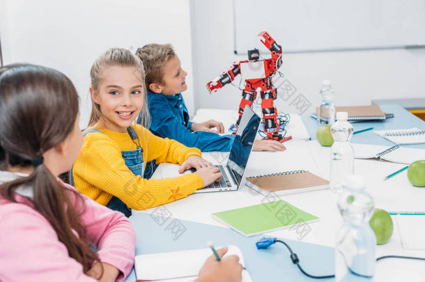 孩子们在笔记本上写字, 在桌上用笔记本电脑, 在阀杆类用红色<strong>机器人</strong>