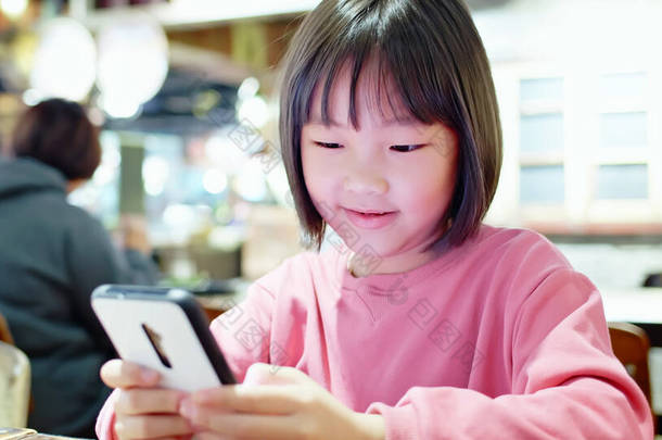 亚洲女孩在餐馆玩手机游戏，开心地笑着