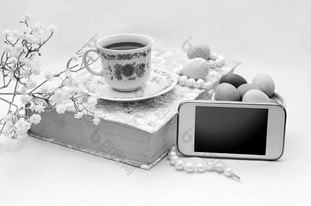 电话与一杯茶和花缎白色背景上的珍珠项链。书、 茶杯、 电话和装饰.