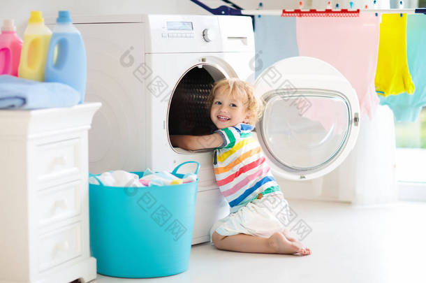 儿童在洗衣房内设有洗衣机或滚筒烘干机。帮助家庭琐事的孩子。现代家庭设备和洗涤洗涤剂在白色阳光的家。烘干机架清洗洗<strong>衣服</strong>. 