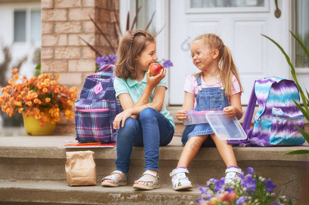 <strong>小学</strong>生与午餐盒在手。有背包的女孩在户外的建筑附近吃水果。<strong>课程</strong>开始。秋天的第一天.
