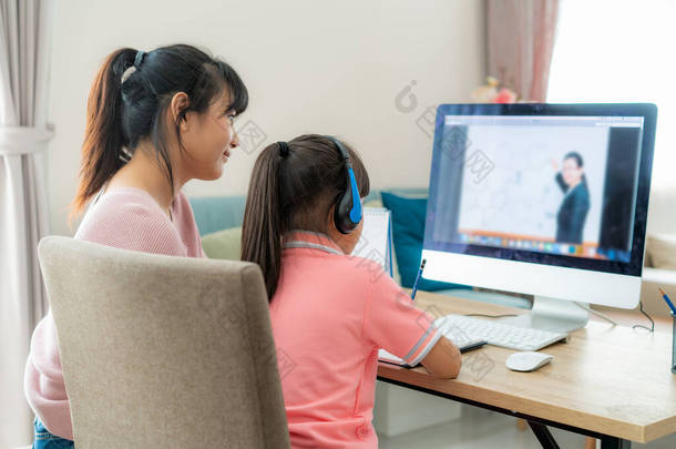 亚洲女学生带着母亲视频会议与老师在家中客厅的电脑上进行<strong>电子</strong>学习。家庭学习和远程学习，在线、教育和互联网.