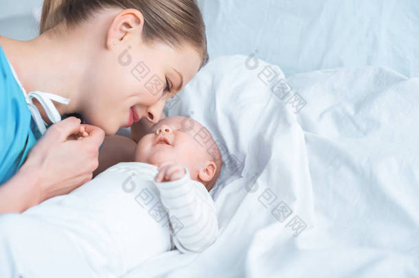 微笑的年轻母亲牵手可爱的新生儿躺在床上 
