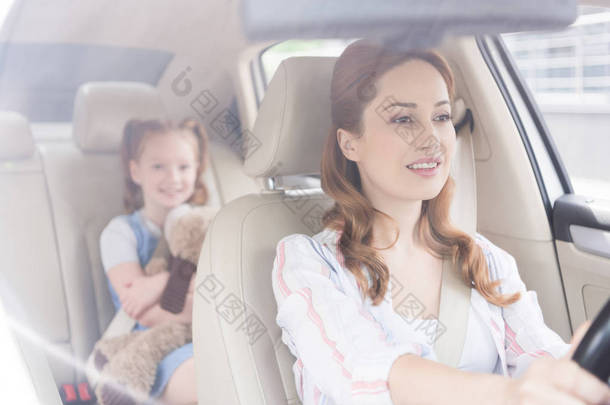 有选择的焦点微笑的母亲驾驶汽车与女儿在乘客位子后面