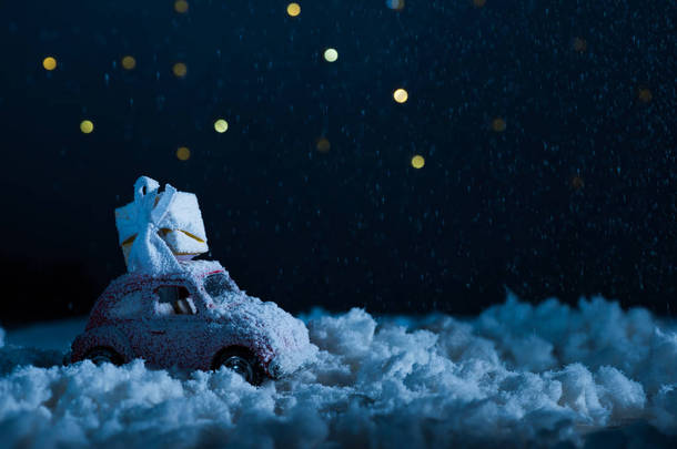 玩具汽车的特写镜头与礼品盒站在雪中的夜晚, 圣诞节概念