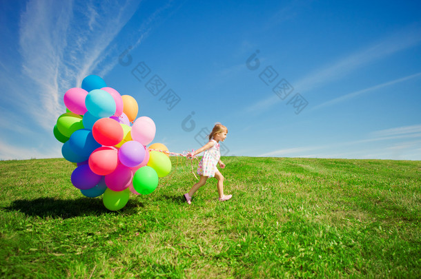小女孩控股五颜六色的气球。孩子在玩在一座绿色