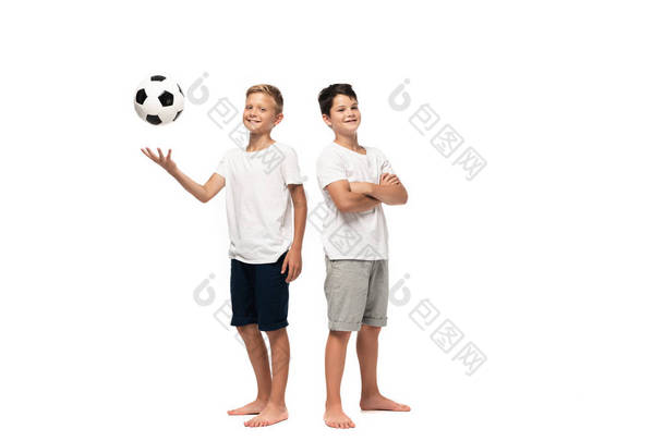 欢快的男孩在笑着的哥哥旁边踢足球，他的胳膊交叉交叉着，背景是白的