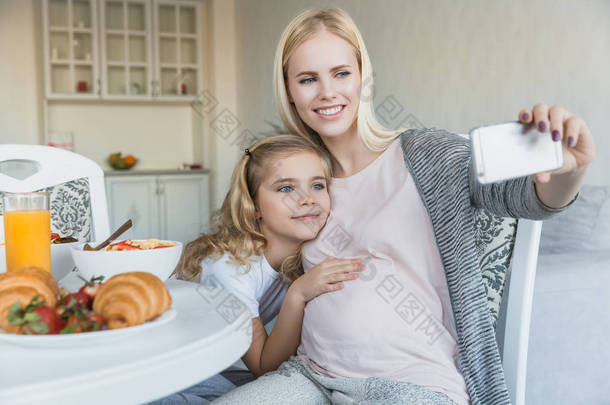 微笑<strong>怀孕</strong>的母亲和女儿在厨房自拍