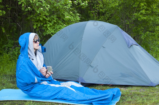 一个男人坐在附近的帐篷睡袋里.