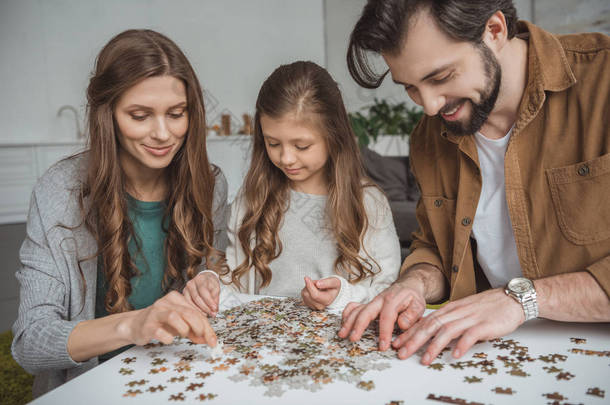 快乐的父母和女儿在餐桌上连接拼图片