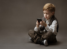 在手机上玩游戏的男孩。孩子坐在灰色的背景上