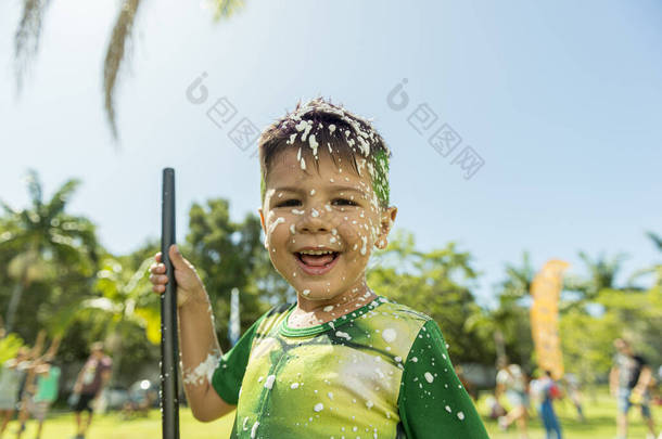 穿著服装的男孩满脸泡沫地微笑着.快乐的男孩在一个美丽的阳光明媚的日子里享受着<strong>嘉年华</strong>的游戏。狂欢节在巴西是一个很有名的聚会.