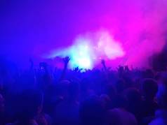 一群人用他们的双手向上在蓝色和紫色场景下空气中烟雾
