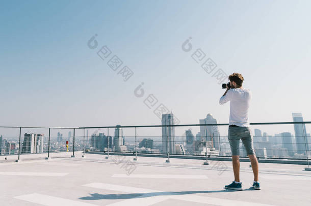 年轻白人白人男子在阳光明媚的一天, 在屋顶上拍摄城市景观照片。摄影嗜好、小工具技术或休闲活动概念。蓝天上的复制空间
