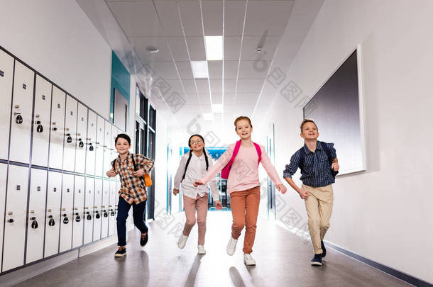 四个兴奋的学生, 放学后背着背包在走廊上跑