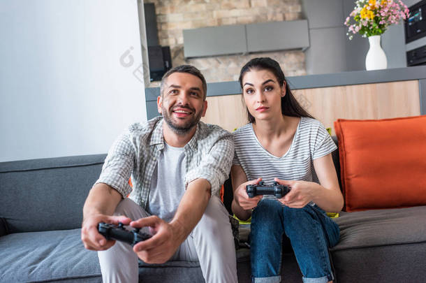 已婚夫妇的肖像与游戏板一起玩电子游戏, 而坐在沙发上在家